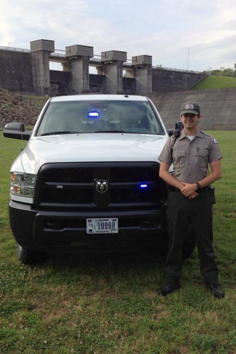 Michael Pracht stands at his patrol vehicle with the Burnsville Dam in the background